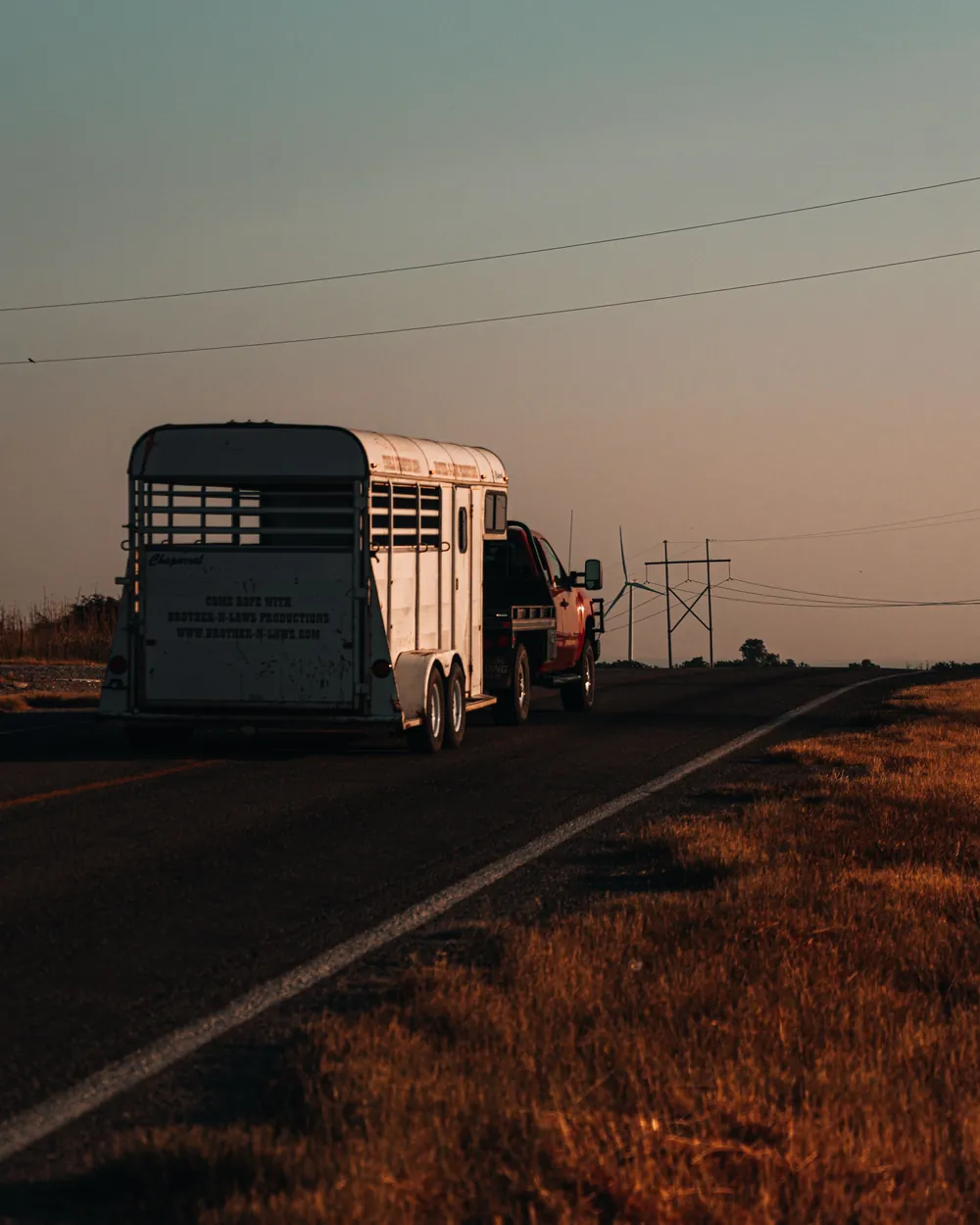 Truck towing a horse trailer down a country highway at dusk